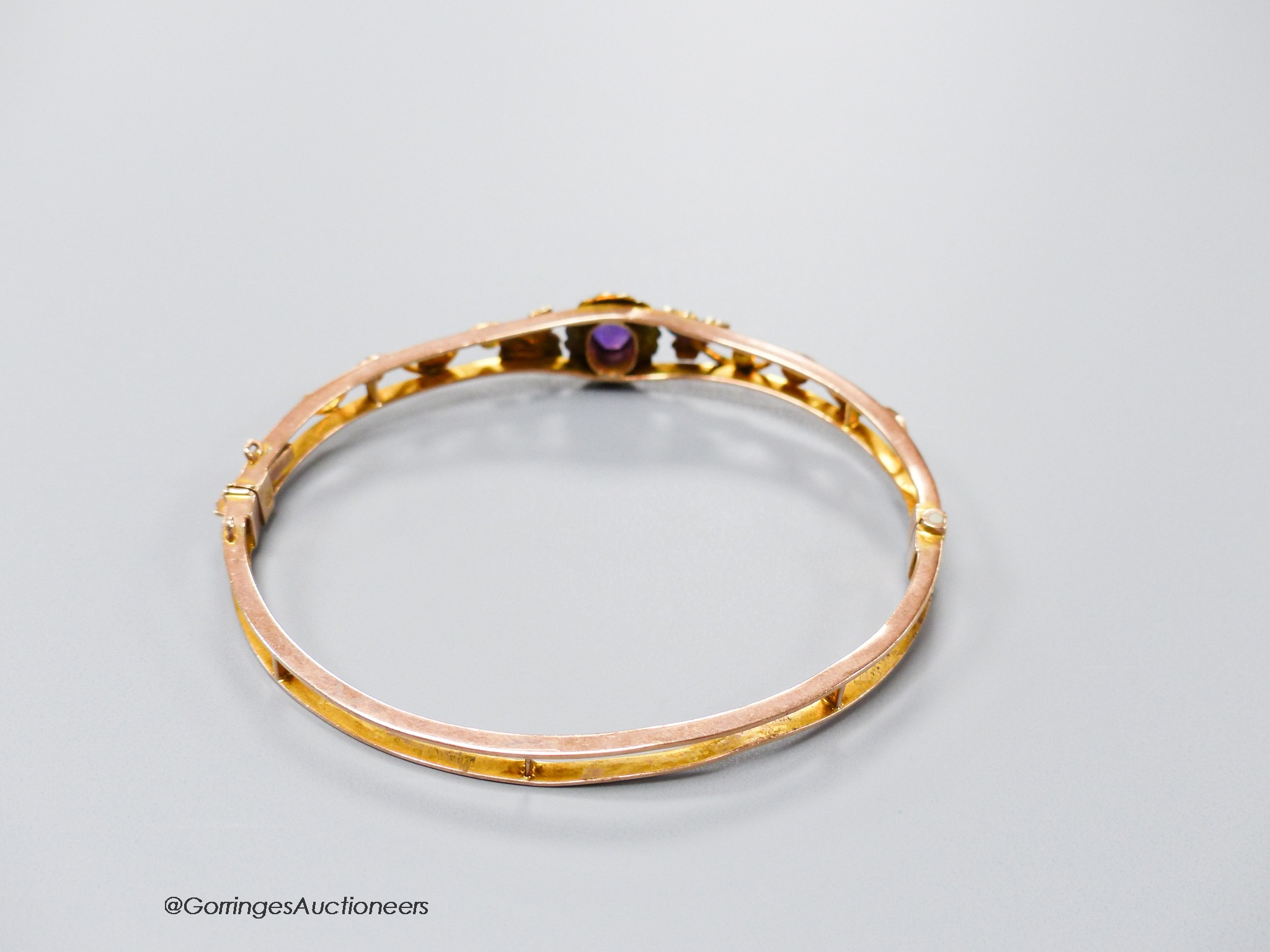 An Edwardian 9ct, amethyst and seed pearl cluster set hinged bracelet, interior diameter 61mm, gross 9.4 grams.